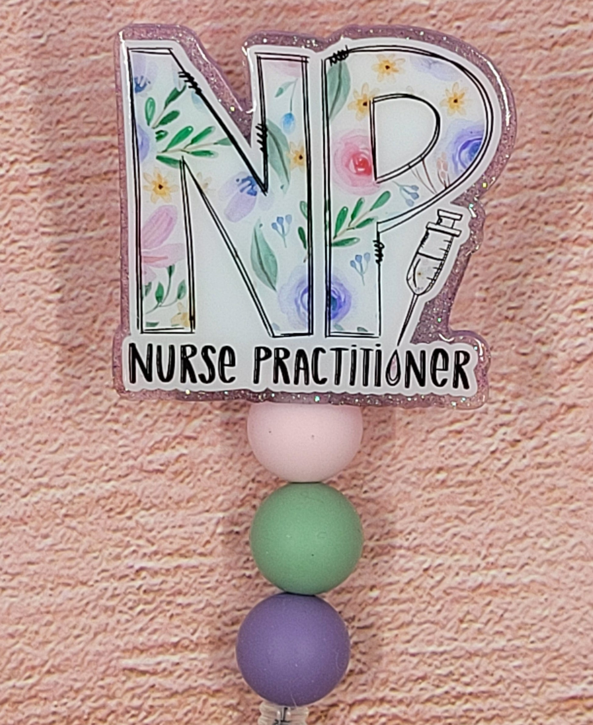 Introducing the new NP Badge Reel, part of our latest collection of Medical Badge Reels available now. Featuring Nurse Practitioner on the front and a purple glitter base adorned with coordinating beads, this Badge Reel is sure to catch the eye.