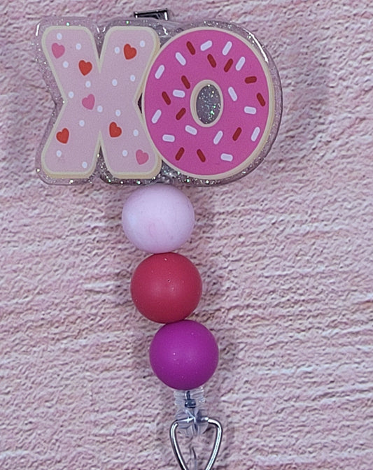 XOXOXO Here we present to you our new Hugs & Kisses Badge Reel. What would Valentine's Day be without them! Featuring a light pink glitter base and coordinated beads, this is the perfect accessory for the holiday season.
