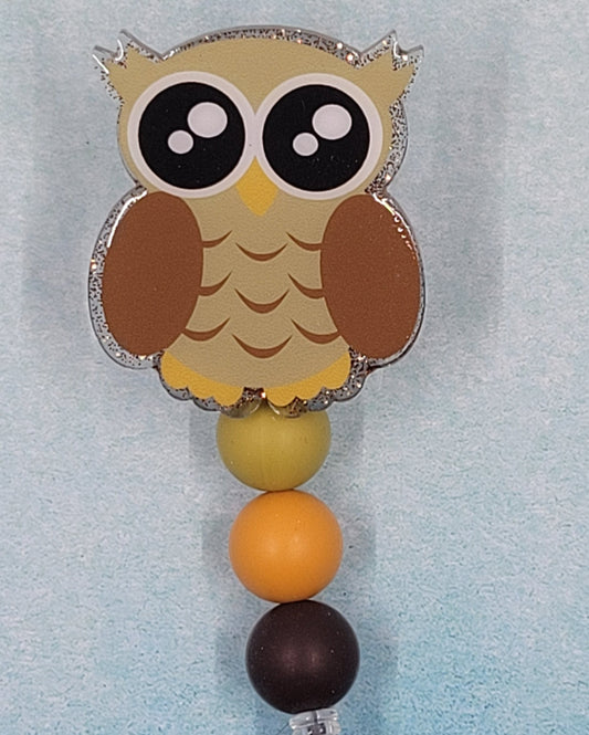 This Badge Reel features a Wise Owl design paired with a shiny brown glitter background. The adorable owl is complemented by three color-coordinated silicone beads for an extra touch of charm. Sure to be a hit with any animal lover.