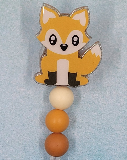 This Badge Reel features a delightful fox design paired with a shiny gold glitter background. The adorable fox is complemented by three color-coordinated silicone beads for an extra touch of charm. Sure to be a hit with any animal lover.