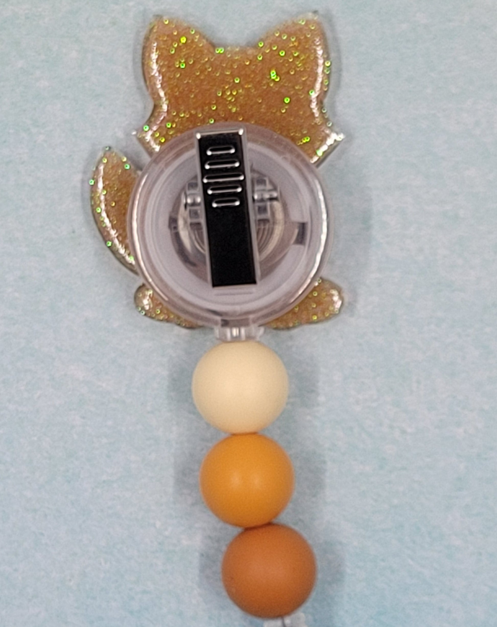 This Badge Reel features a delightful fox design paired with a shiny gold glitter background. The adorable fox is complemented by three color-coordinated silicone beads for an extra touch of charm. Sure to be a hit with any animal lover.