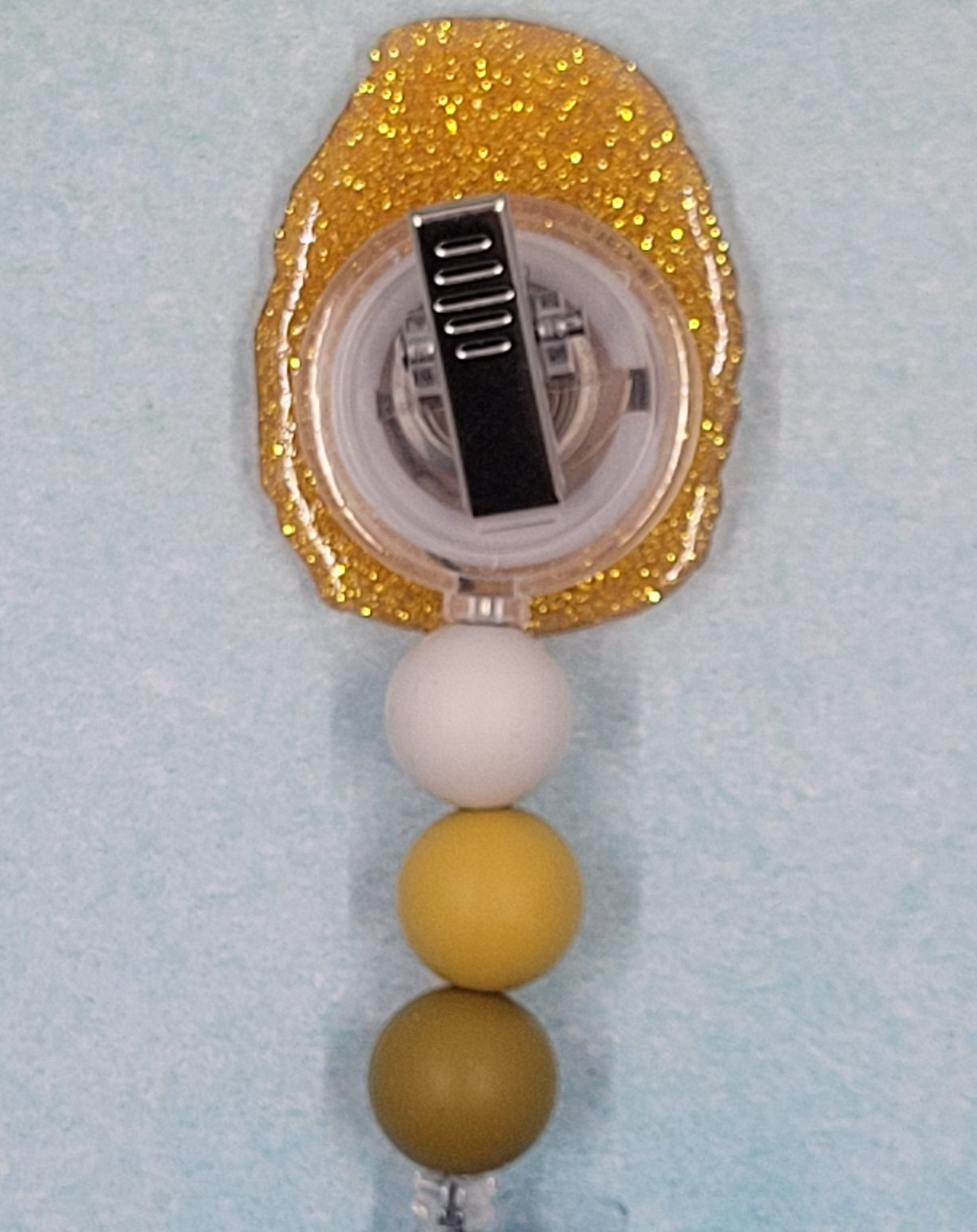 Nug Life! Only thing missing is your dipping sauce. This Chicken Nugget Badge Reel looks good enough to eat. Looks like someone already snuck a bite. Golden brown in color with matching glitter background, 3 color coordinated beads finish this tasty treat.