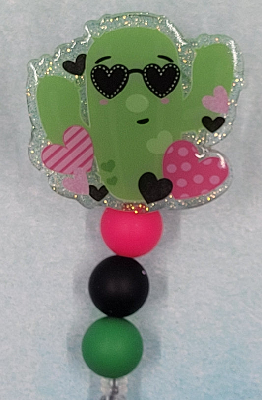 Love can be a Prickly thing, even so with a cactus! This cool cactus is wearing heart shaped glasses bordered with various hearts and overlays a green glitter background. Finished off with 3 silicone color coordinated beads. Great for the plant enthusiast.