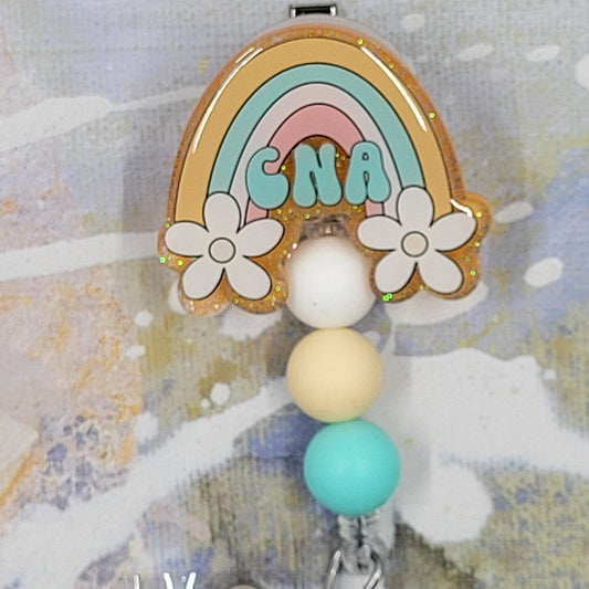 Introducing the new CNA Badge Reel, part of our latest collection of Medical Badge Reels available now. Featuring CNA in blue lettering in front of a rainbow with white daisy's and a yellow gold glitter base adorned with coordinating beads, this Badge Reel is sure to catch the eye.