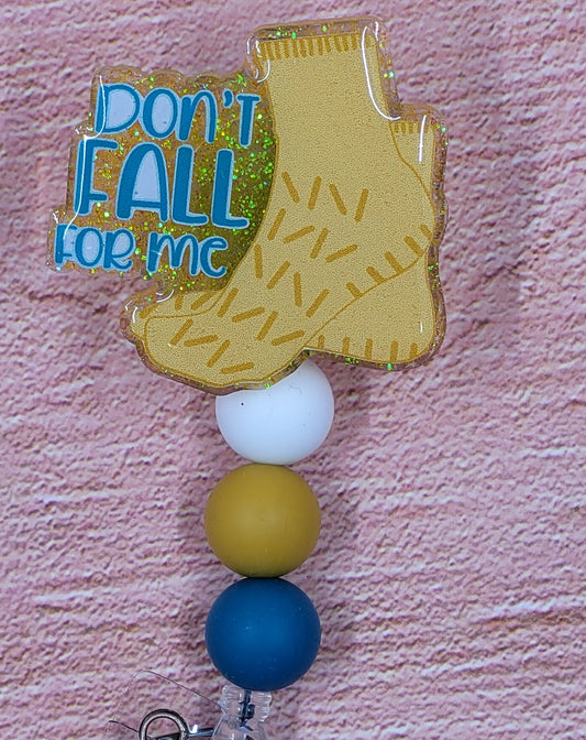 If you have ever spent any time as a patient in a hospital...you know what these are....GRIPPY SOCKS. So warm and comforting and all those rubber grips to help keep you from falling! This badge reel depicts those socks with a yellow glitter base. The phrase Don't Fall For Me in blue lettering and 3 color coordinated silicone beads.