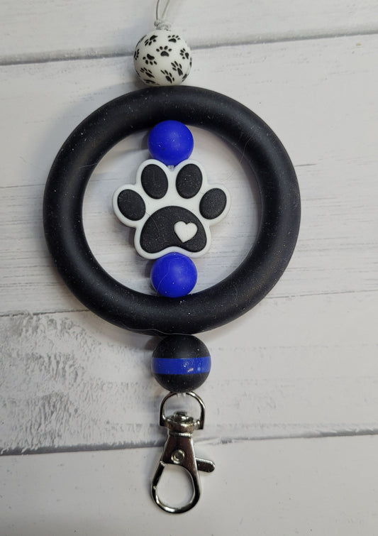 Need a custom Freshie Hanger? Here is a silicone beaded hanger we like to call Police K9. A unique design featuring all silicone beads. A black ring with a Dog Paw main focal bead flanked with blue beads and a dog paw print outer bead on 1 side and a back the badge bead on the other to finish the look. Attaches quickly to any one of our many Freshies so you can easily hang it from your rear view mirror.