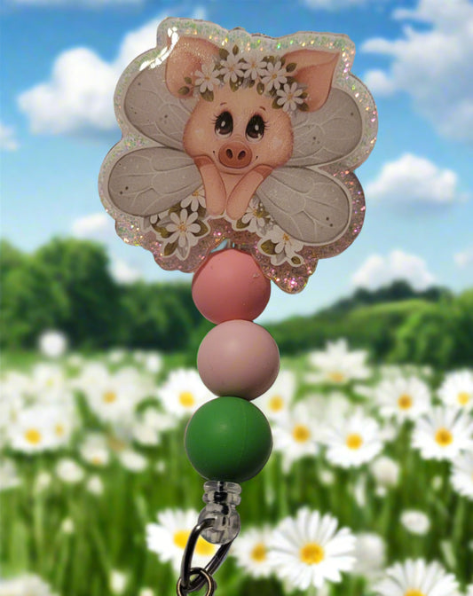 Unleash your inner whimsy with this delightful Badge Reel starring a charming little Fairy Piggy, complete with flower-festooned wings and a sparkling pink backdrop. And don't forget the adorable trio of matching silicone beads for a dash of extra charm. Perfect for all animal enthusiasts!
