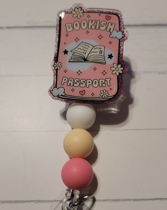 Know a librarian or a book worm that can use a Badge Reel. Here we have our Bookish Passport. Books open the door to your imagination to go or be anyone without having to actually get a real passport. A pink theme here with an open book on the front, purplish pink glitter back, and 3 color coordinated silicone beads to finish the look.