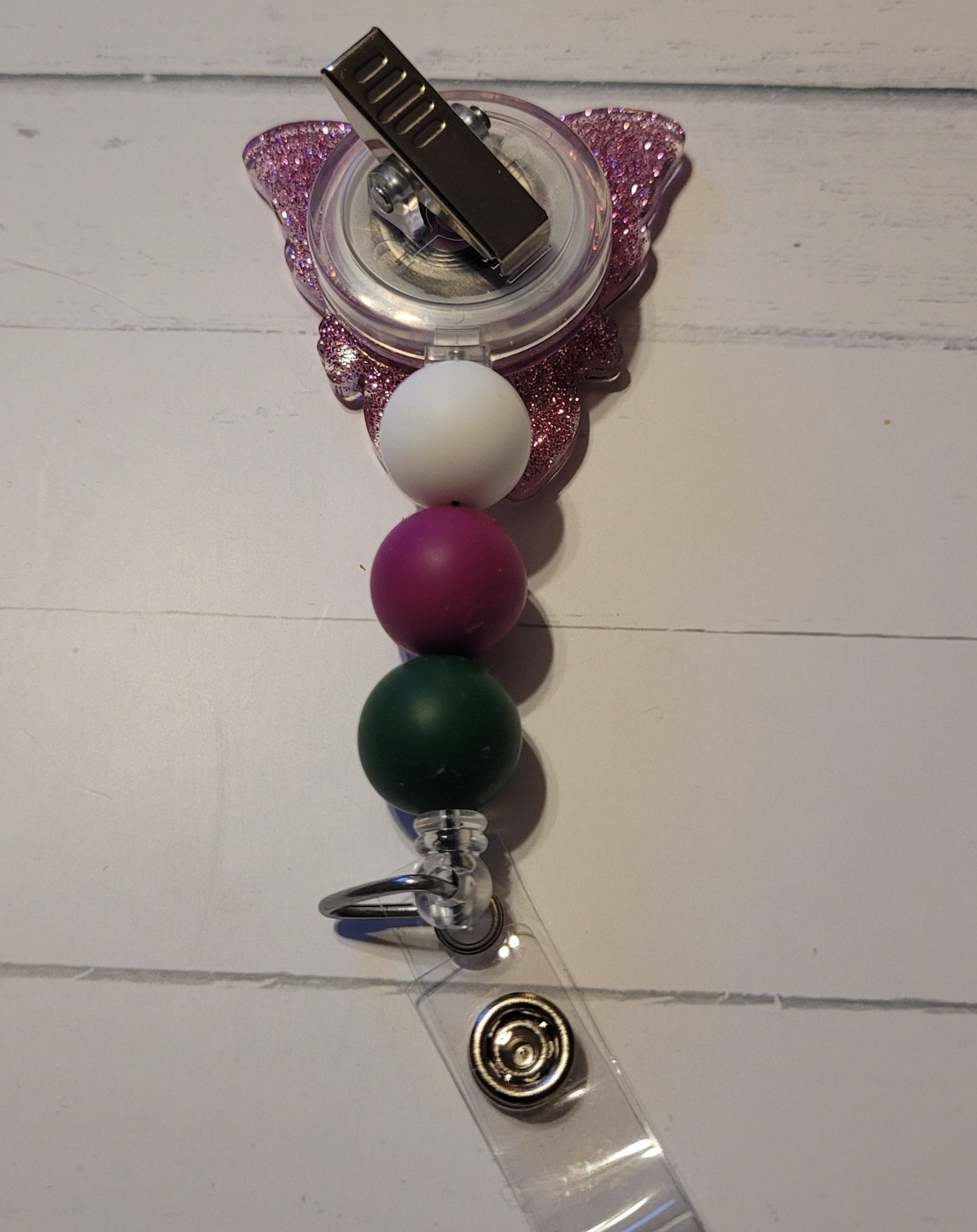 This Badge Reel features a beautiful moth with sunflower images on each wing and a shiny purple glitter background. The colorful moth is complemented by three color-coordinated silicone beads for an extra touch of charm. Sure to be a hit with any animal lover.