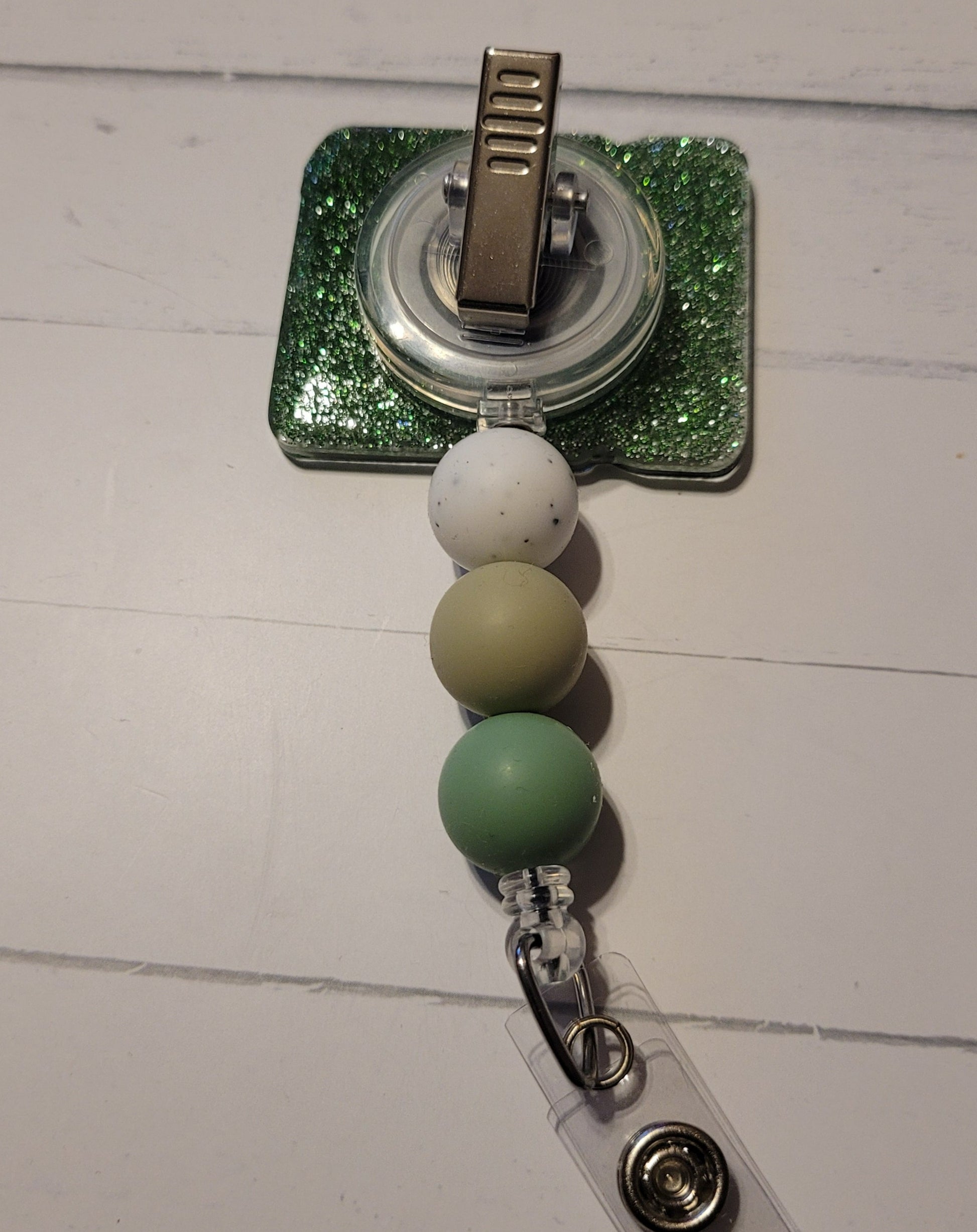 This badge reel promotes self-expression with the message "Be You." The bold lettering in various shades of green pops against a glittery green background. It also features three coordinating silicone beads for added flair.