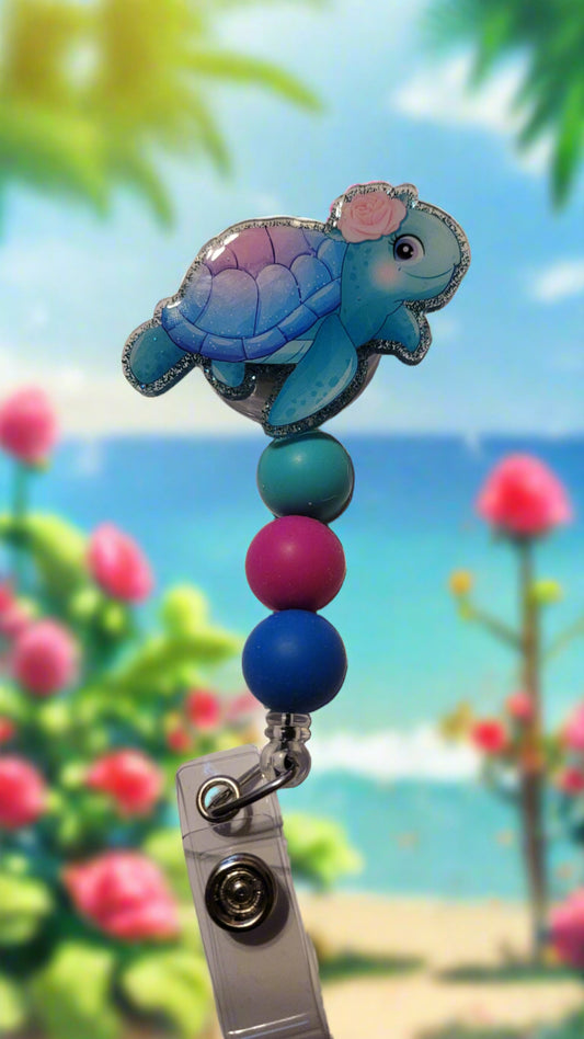 This delightful badge reel features a cheerful blue turtle with a bright pink rose atop its head. It also boasts a sparkly blue background and three cute matching silicone beads for added charm. An absolute must-have for all animal lovers!