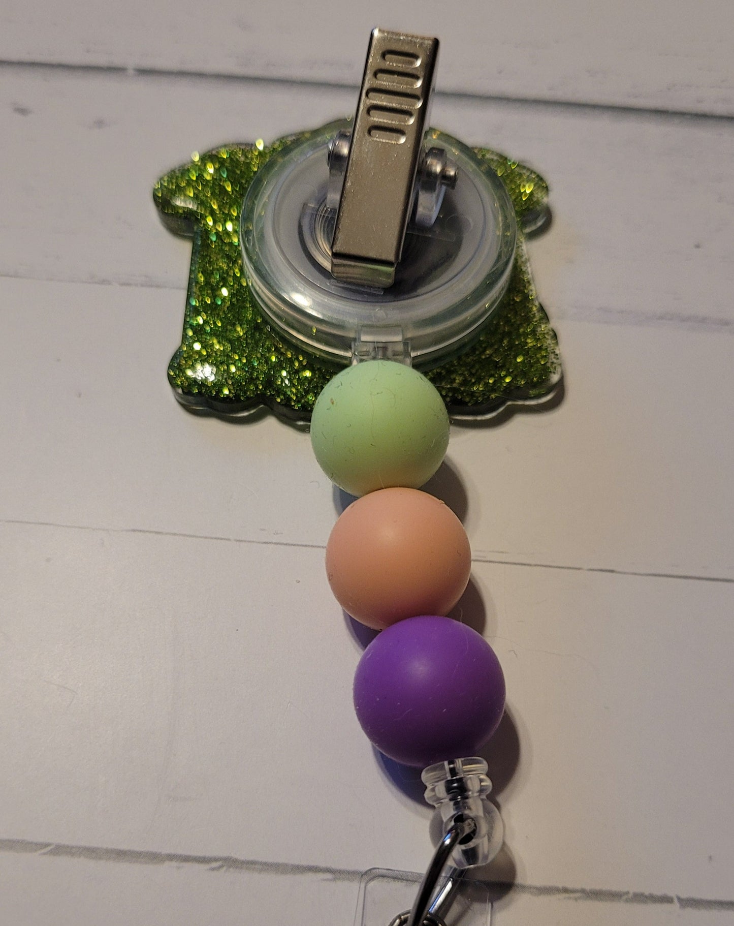Ever wonder what really to the Dinosaurs? This fun Badge Reel playfully suggests they were beamed up to spaceships by aliens. 3 different ships beaming up various dinosaurs with a green glitter background and 3 fun colored silicone beads to finish the look.
