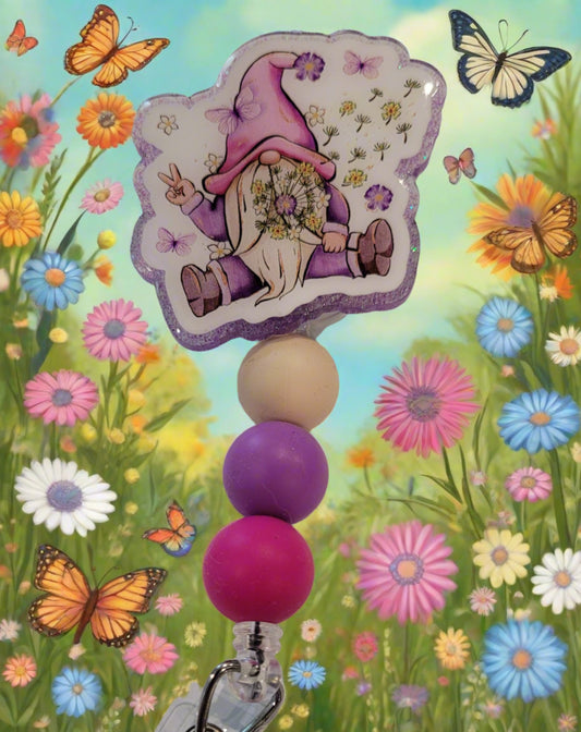 Peace Out Gnome. This cool dude is throwing the peace sign as he sits among flowers and butterflies. Just a happy go lucky kind of badge reel. Also features a purple glitter back and 3 silicone color coordinated beads. Peace Dude!