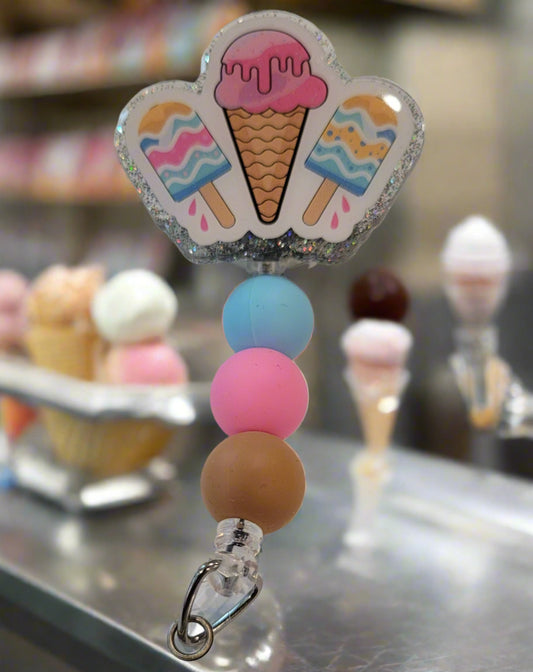 I scream you scream we all scream for Ice Cream! Beat the heat of summer with the time-honored treat of the classic ice cream cone. This acrylic badge reel features 3 tasty treats with a shimmering glitter back and color coordinating silicone beads to finish the look.
