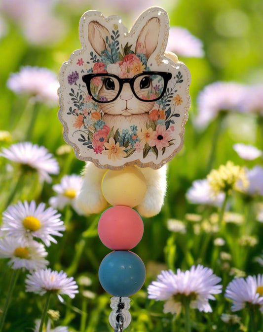 Unleash your inner whimsy with this delightful Badge Reel starring a charming little glasses wearing Bunny, Complete with a setting of wildflowers and a light orange glitter back. And don't forget the adorable trio of matching silicone beads for a dash of extra charm. Perfect for all animal enthusiasts!
