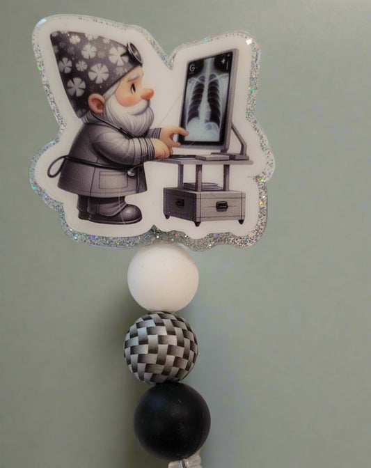 Introducing the new Gnome X-Ray Tech Badge Reel, part of our latest collection of Medical Badge Reels available now. Featuring a cute Gnome examining an X-Ray dressed in shades of gray and a silver glitter base adorned with silver black &amp; white 3d visual bead and s more color coordinating beads, this Badge Reel is sure to catch the eye.