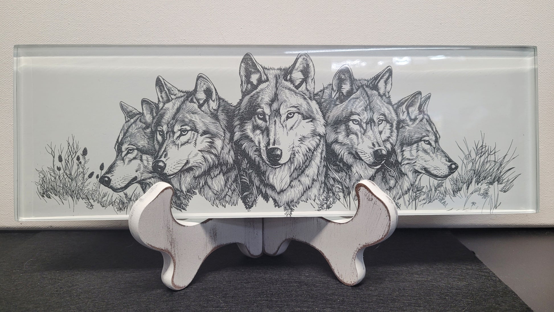 This basic glass wall tile as been transformed into a beautiful laser engraved wolf collage image. The fine detail from the laser really shines through on the white background. Measuring 4" tall x 12" wide and 1/4" thick, this tile is a strong sturdy piece. Black felt backing allows you to display flat on a table or use the white washed wooden easel that comes with it. You could even use in a remodel and put in a tiled wall if you so choose or display it for yourself or a gift for family or friend,