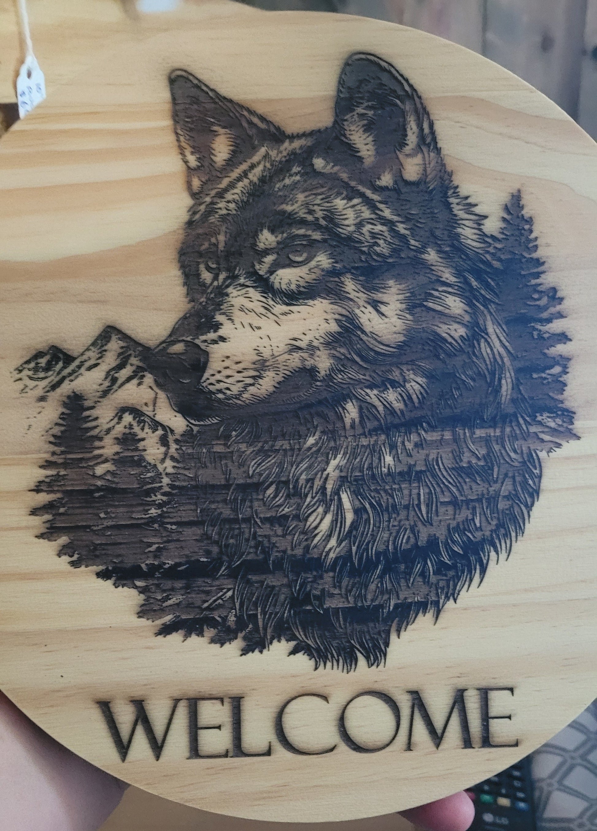 Here we took a 5/8" thick x 10" round pine board and laser engraved a Wolf with a mountain range in the background. Also has they word "Welcome" under the main image. Sealed with multiple coats of clear poly to help protect the finish. 1 sawtooth and 2 nails included for hanging.