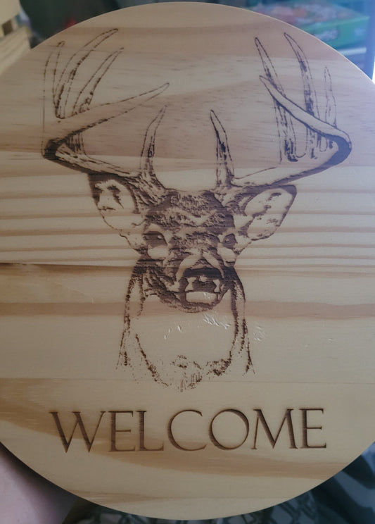 Here we took a 5/8" thick x 10" round pine board and laser engraved a Whitetail Buck. Also has they word "Welcome" under the main image. Sealed with multiple coats of clear poly to help protect the finish. 1 sawtooth and 2 nails included for hanging.