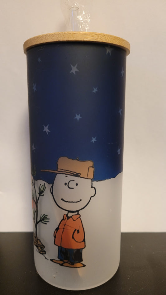 It's a Peanuts Christmas. Charlie Brown & Snoopy stand outside admiring the iconic Charlie Brown Tree. This image is sublimated onto a glass can tumbler and comes with a straw and bamboo lid.