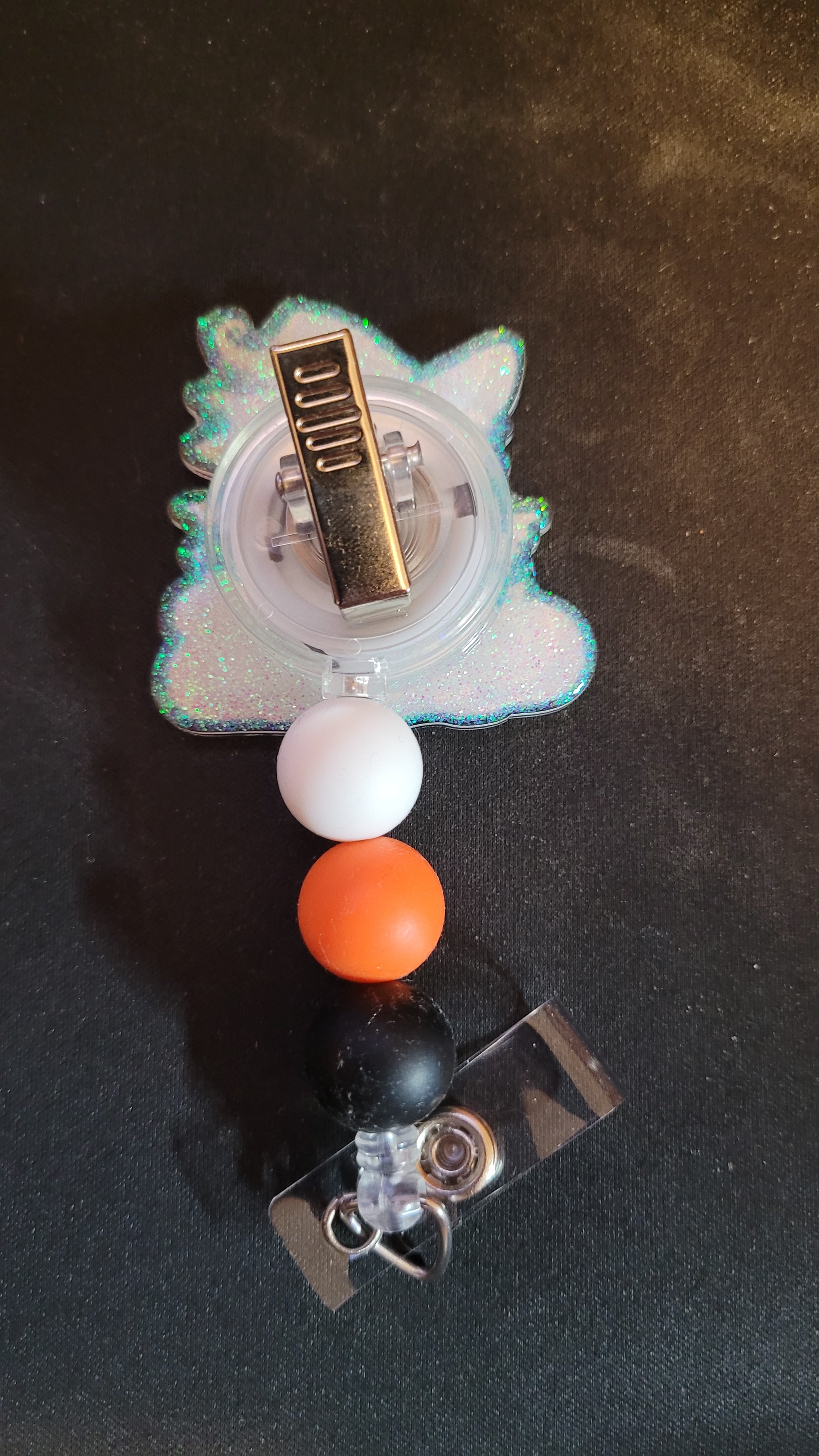 This pumpkin acrylic badge reel features a frazzled black witch cat planning his next scary trick.... or treat. A shiny glitter base pops through and is finished with 3 color coordinated silicone beads.