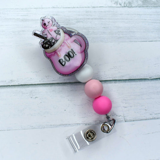 This sleek acrylic badge reel features our beloved Voo Doo character, perched atop a pink cup containing a warm cup of hot chocolate. The design is complete with a white silicone bead and two varied shades of pink.