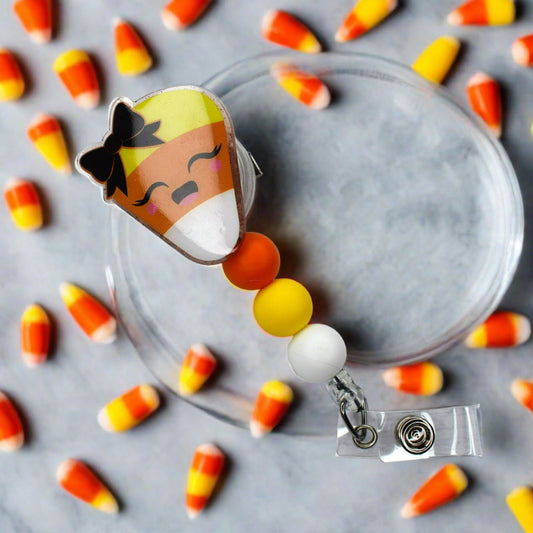 This eye-catching candy corn badge reel is sure to evince delight from viewers with its charming bow and yellow, white and orange silicone beads.