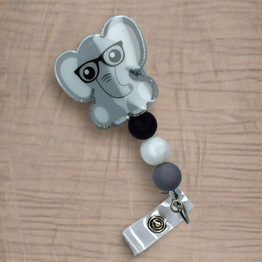 This highly distinctive animal lover acrylic badge reel, featuring a cartoon elephant with glasses, is complete with three grey, black and white pearl-finished silicone beads.