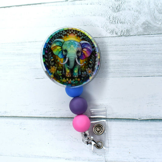 This acrylic badge reel, featuring an elephant with stained glass background, is a glorious visual. A combination of blue, purple, and pink silicone beads provides a stunning finish.