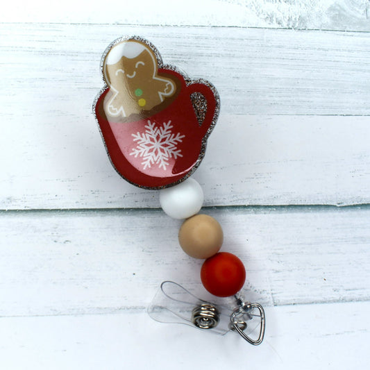 This acrylic badge reel boasts a delightful red mug of hot cocoa with a happy gingerbread man cookie. White cream & red silicone bead finish the toppings on this winter favorite drink.