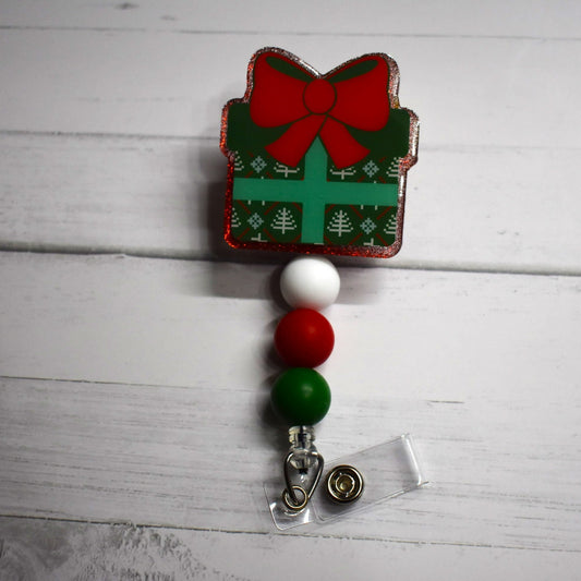 Everybody loves getting a gift. Here we have badge reels in the classic Gift Box design with a big red bow. 4 options to choose from that include red or green glitter back grounds and a red or green color gift wrapping. All have the same white red and green silicone accent beads to finish the look.