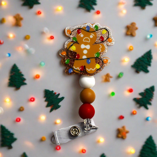 This acrylic Gingerbread Man has found himself all tangled up in a string of lights. This badge reel makes a festive addition to your look with a golden glitter background and white brown and red silicone accent beads. Ideal for celebrating the Christmas Holidays.