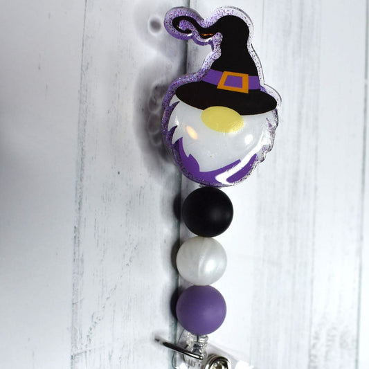 This acrylic Gnome Witch badge reel features black pearl and purple silicone accents, and is the perfect choice for Halloween festivities.