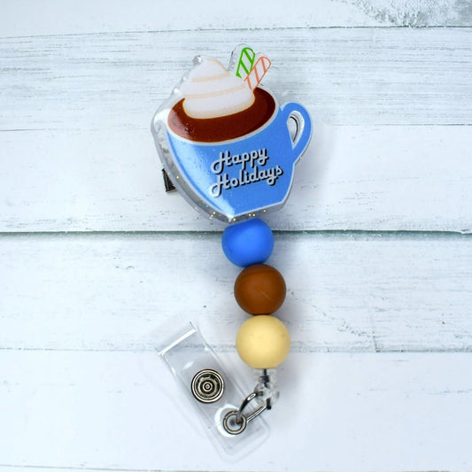 This acrylic badge reel boasts a delightful blue mug of hot cocoa and Happy Holidays across the front. Matching blue tan and cream silicone beads finish the toppings on this winter favorite drink.