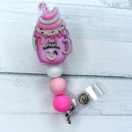This acrylic badge reel features a pink Halloween mug filled with tasty ice cream and topped with a white silicone bead and 2 different pink shaded beads. 