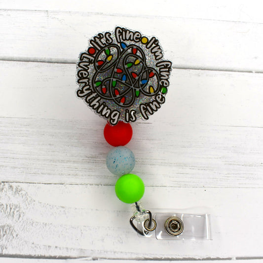 It's Fine, I'm Fine, Everything's Fine. We have all been there. Now your badge reel is proof. A clear glitter base sparkles though with a tangled mess of lights. 3 color coordinating silicone beads finish the look.