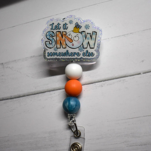 Let It Snow.... Somewhere Else! For those who frown upon snow this badge reel is for you. A snow man ornament representing the letter O in Snow is front and center here with a blue glitter back ground finished with white peach and a blue marble silicone beads.
