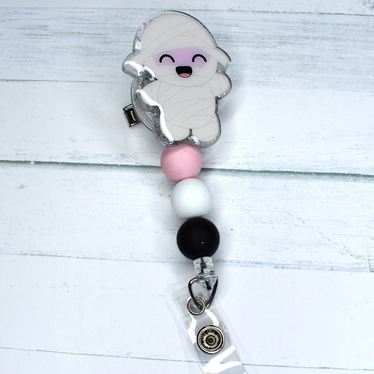This Mummy acrylic badge reel is designed to evoke Halloween spirit. It features classic white, pink, and black silicone beads, perfect for ghost ghouls and MUMMIES alike!