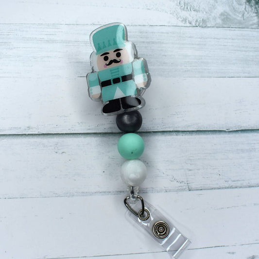 This acrylic Gnome Nutcracker in teal uniform badge reel features 2 different combinations of silicone bead accents, and is the perfect choice for Christmas festivities.