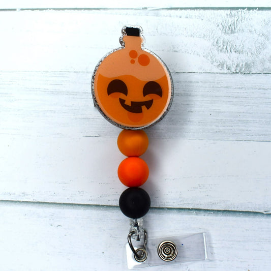 Halloween Pumpkin Potion, what spell can you cast. This acrylic badge reel has a smiling carved pumpkin face on a flask of potion. Festive colored Halloween silicone matching beads finish the spell.