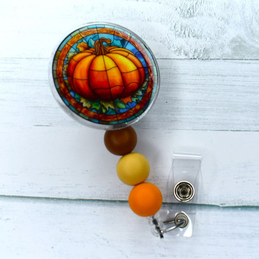 Fall Harvest heralds this eye-catching acrylic badge reel featuring a pumpkin on a stained glass background, accented by three silicone beads in earthy hues of brown, tan, and orange.
