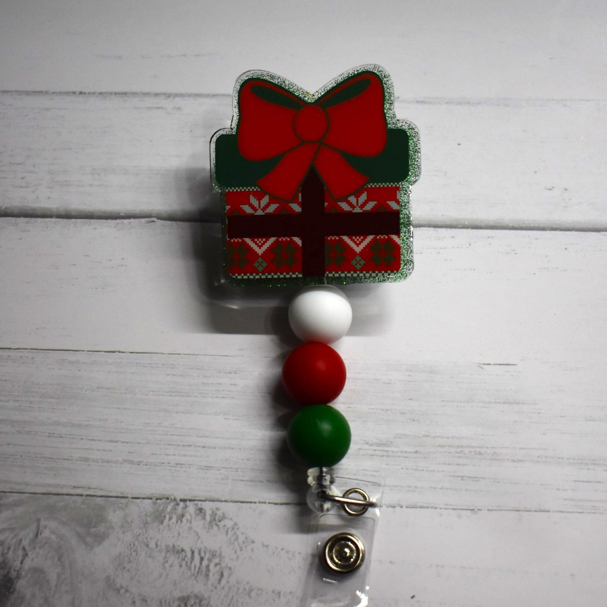 Everybody loves getting a gift. Here we have badge reels in the classic Gift Box design with a big red bow. 4 options to choose from that include red or green glitter back grounds and a red or green color gift wrapping. All have the same white red and green silicone accent beads to finish the look.