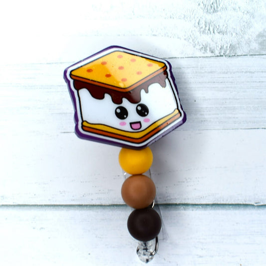 Camping out often leads to enjoying the classic treat of smores! This attractive acrylic badge reel offers a cheerful depiction of a smore, complete with yellow-tan and chocolate-brown silicone beads.