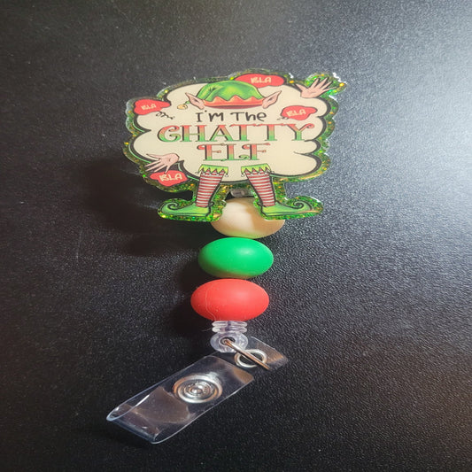 I'm The Chatty Elf badge reel is here for all to talk about. A fun elf clothing image with multiple Bla Bla Bla word clouds floating around. Features a green glitter back and 3 color coordinated silicone beads.