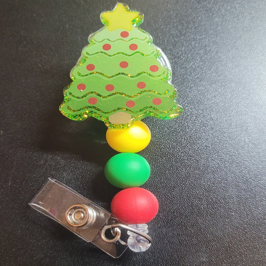 Tis the season for the lighting of the Christmas Tree. This badge reel makes a festive addition to your look with red ornaments, a gold glitter background and 3 silicone accent beads. Ideal for celebrating the Christmas Holidays.