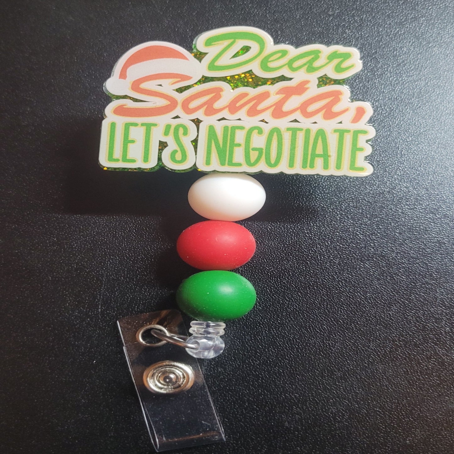 Not sure which of Santa's lists you made? Negotiate! Just in time for the holidays we bring you the Dear Santa Let's Negotiate badge reel. A green glitter back and 3 silicone matching beads An excellent choice for a stocking stuffer.