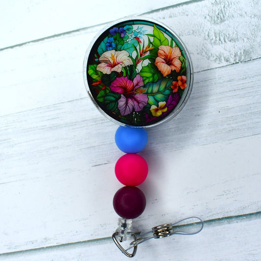 This acrylic badge reel includes a unique take on the stained glass design, featuring various flowers with coordinating silicone accent beads in shades of blue, pink, and purple.