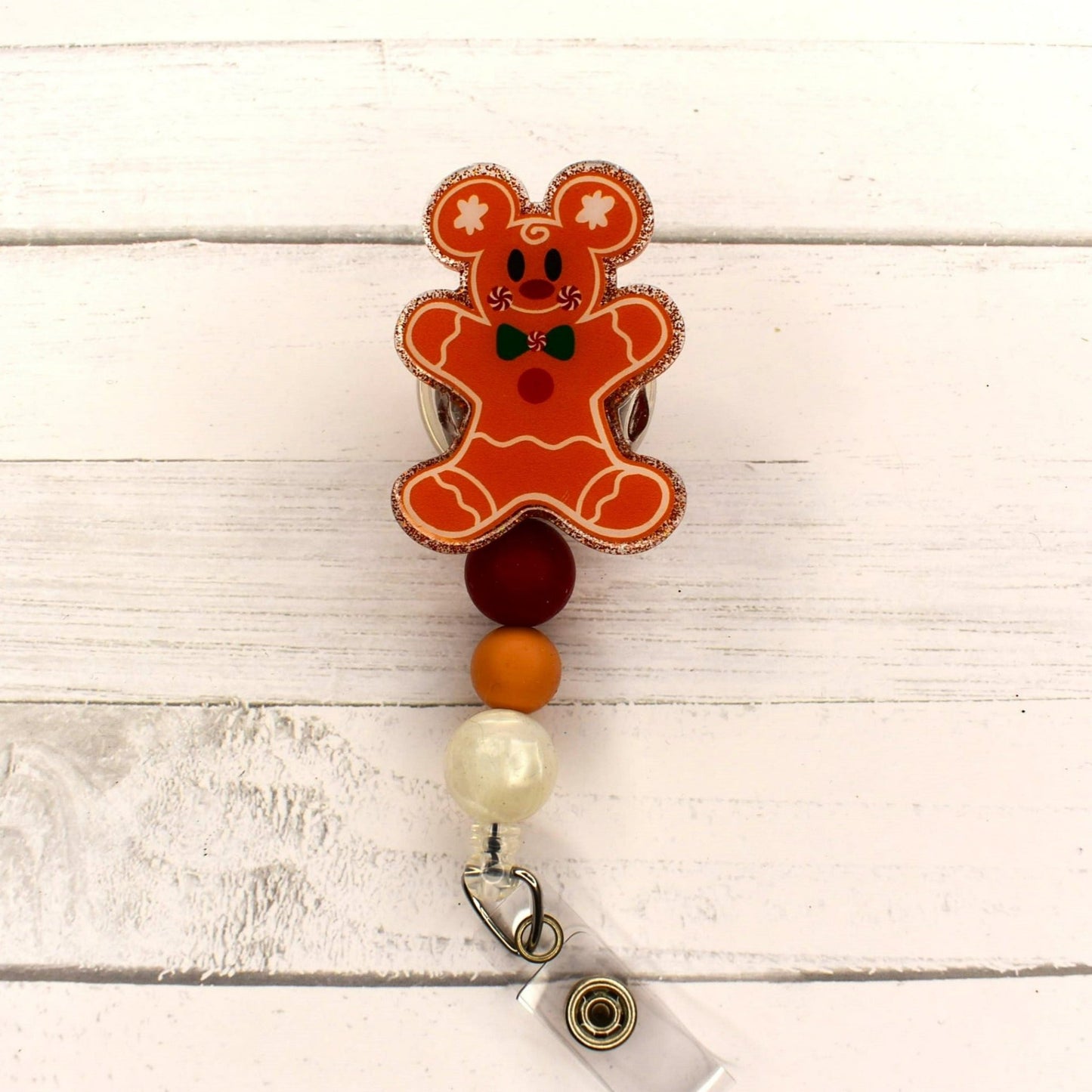 This badge reel features a cute Gingerbread Bear with a glitter base and 3 silicone color coordinated beads. 2 versions available. 1 has a pretty red bow in her hair and the other does not.