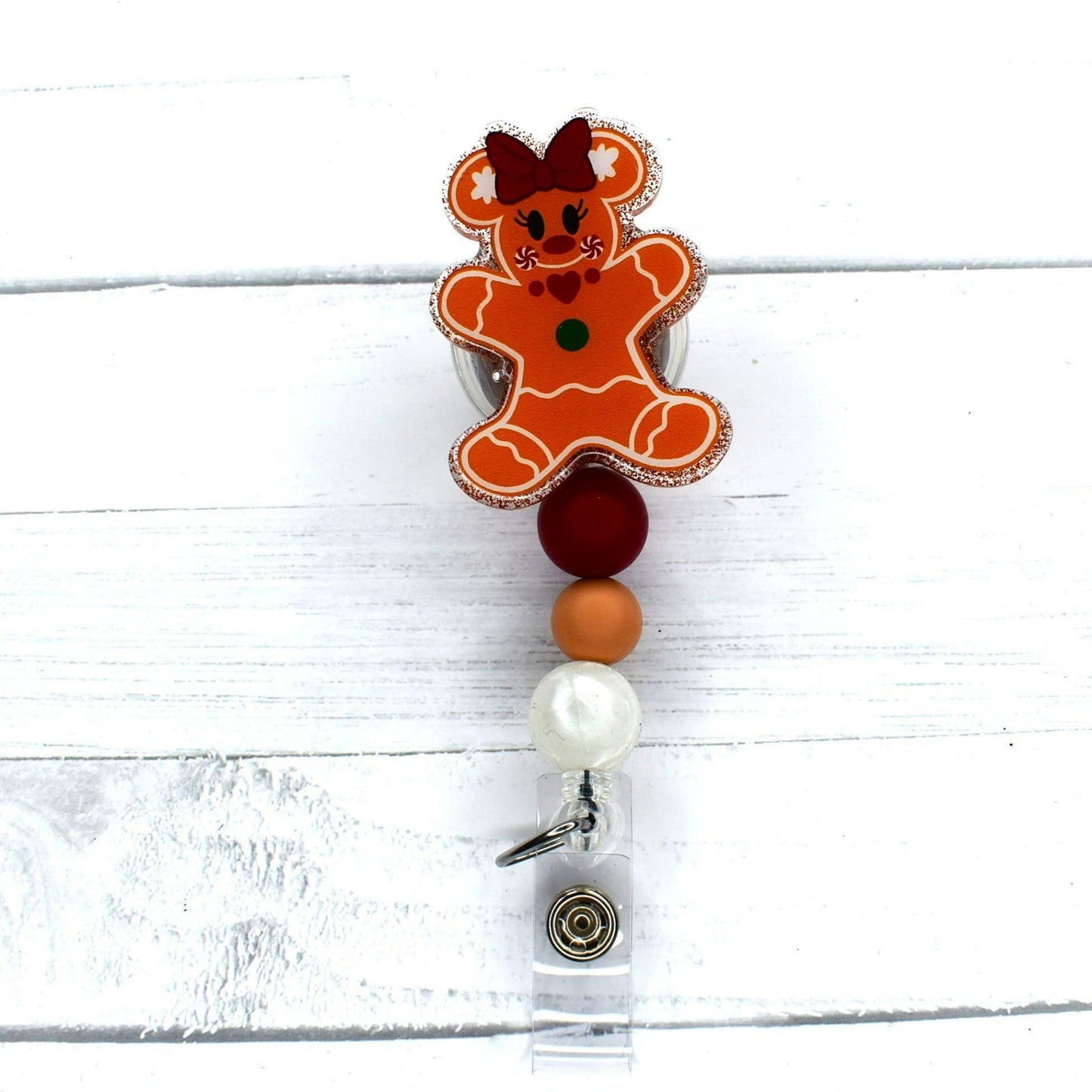 This badge reel features a cute Gingerbread Bear with a glitter base and 3 silicone color coordinated beads. 2 versions available. 1 has a pretty red bow in her hair and the other does not.