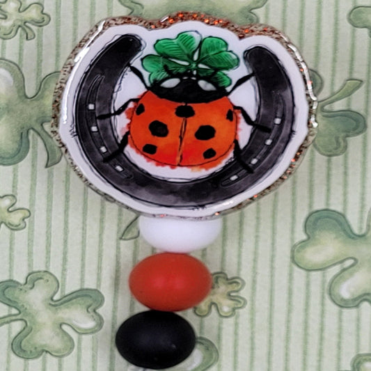 Felling Lucky? How about Luck X 3 lucky! This badge reel features 3 of the more popular lucky things. A horseshoe, a lady bug and of course a 4 Leaf Clover. A brilliant red glitter base and 3 silicone color coordinated beads finish the look.